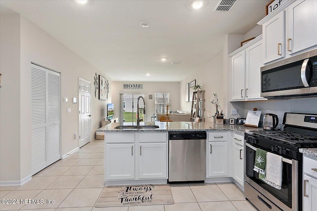 kitchen with light stone countertops, sink, stainless steel appliances, kitchen peninsula, and white cabinets