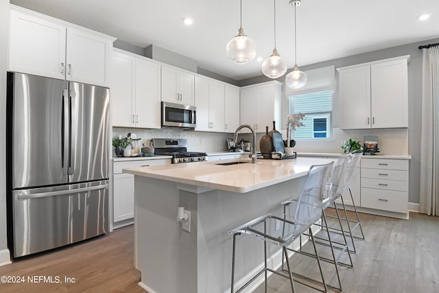 kitchen with appliances with stainless steel finishes, sink, a center island with sink, white cabinets, and light hardwood / wood-style floors