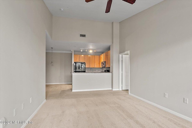 unfurnished living room with ceiling fan, light colored carpet, a towering ceiling, and sink