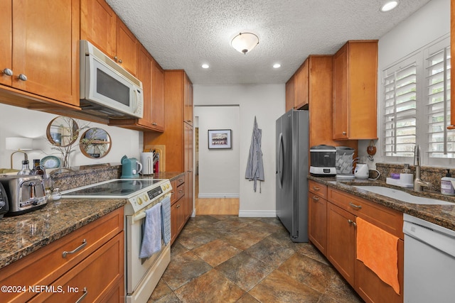 kitchen with a textured ceiling, dark stone countertops, white appliances, and sink