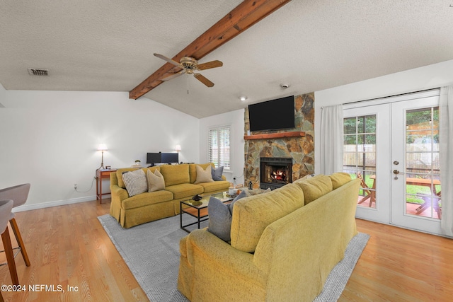 living room featuring french doors, light wood-type flooring, a textured ceiling, vaulted ceiling with beams, and a stone fireplace