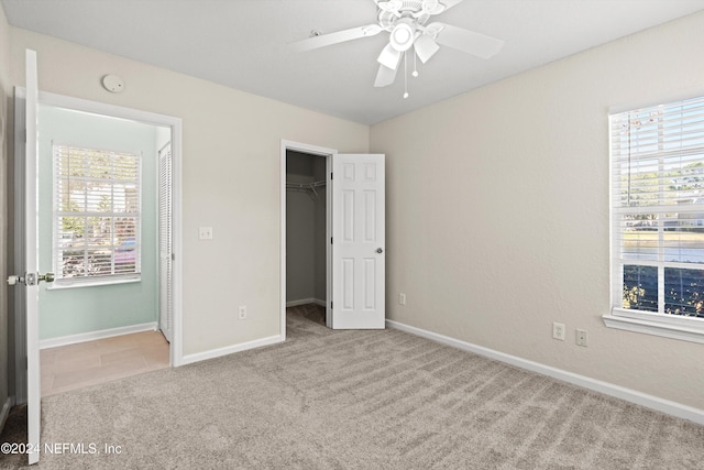 unfurnished bedroom with ceiling fan, a spacious closet, light carpet, and a closet