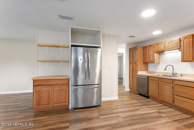 kitchen with light wood-type flooring, stainless steel appliances, backsplash, and sink