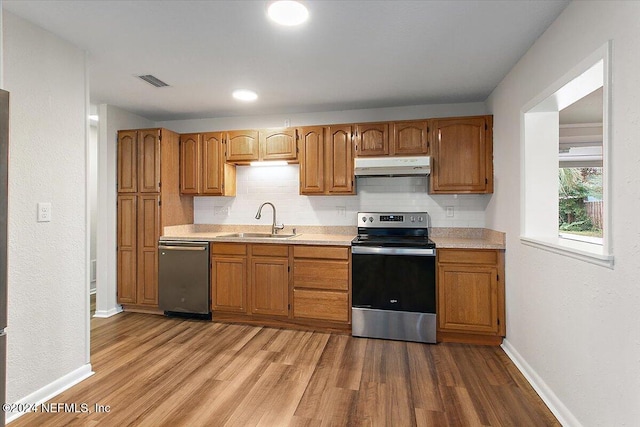 kitchen featuring appliances with stainless steel finishes, light hardwood / wood-style floors, tasteful backsplash, and sink