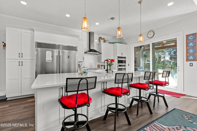 kitchen with white cabinets, wall chimney range hood, stainless steel appliances, and a large island with sink