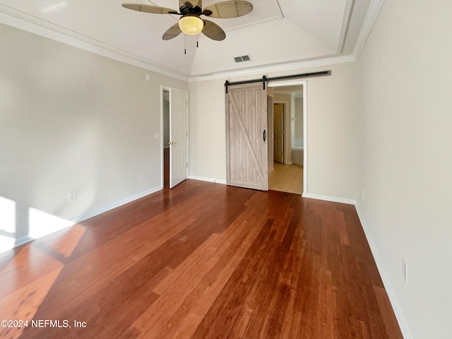 spare room with a barn door, crown molding, hardwood / wood-style floors, and ceiling fan