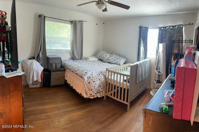 bedroom with multiple windows, ceiling fan, dark hardwood / wood-style flooring, and a crib