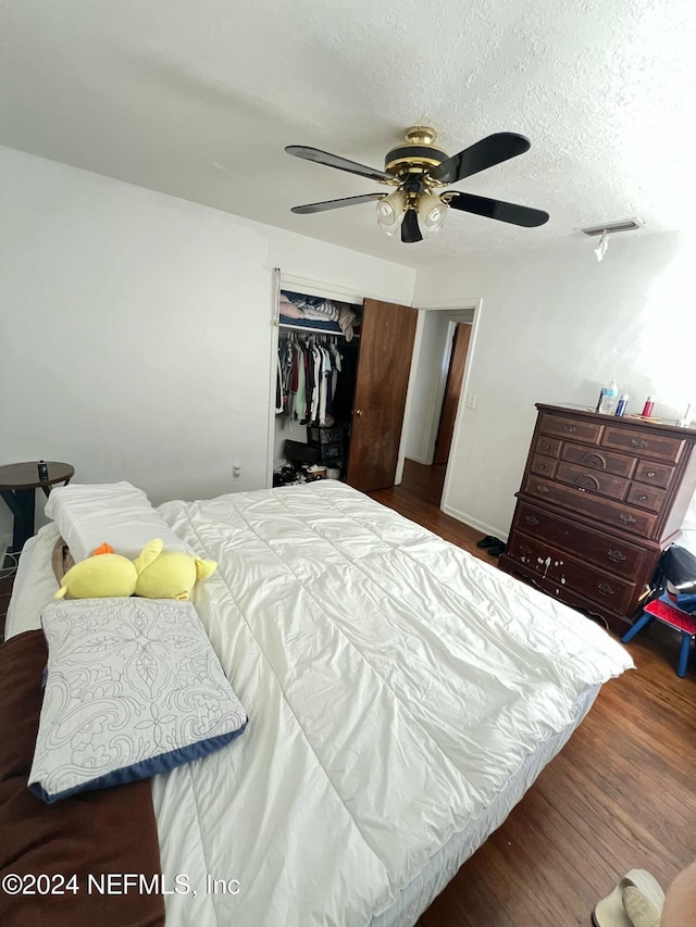 bedroom with ceiling fan, dark hardwood / wood-style flooring, a textured ceiling, and a closet