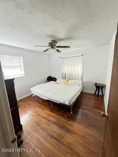 bedroom with a textured ceiling, ceiling fan, and dark hardwood / wood-style floors