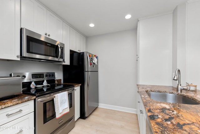 kitchen with sink, dark stone countertops, light wood-type flooring, appliances with stainless steel finishes, and white cabinetry