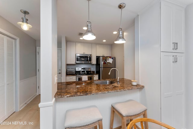 kitchen featuring sink, dark stone countertops, light wood-type flooring, white cabinetry, and stainless steel appliances