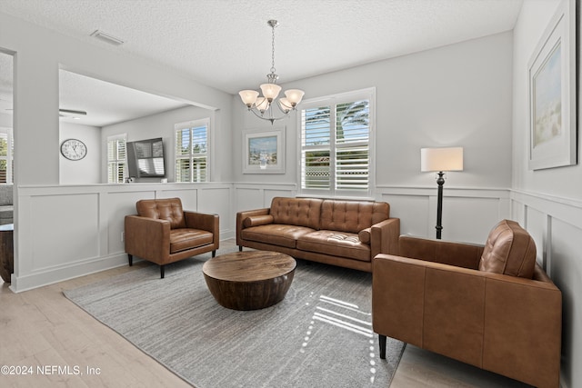 living room with light hardwood / wood-style floors, a textured ceiling, and a notable chandelier