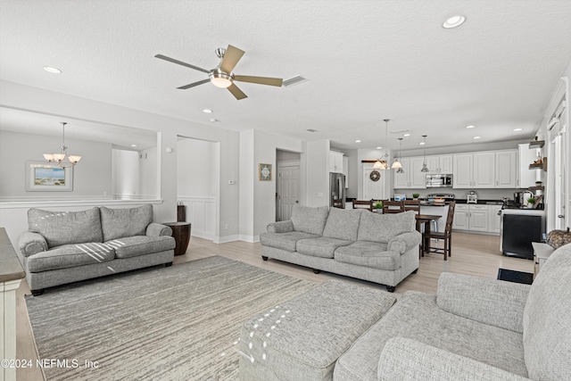 living room with ceiling fan with notable chandelier, light hardwood / wood-style floors, and a textured ceiling