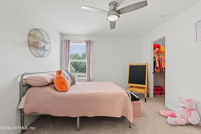 carpeted bedroom featuring a walk in closet, ceiling fan, a closet, and a textured ceiling