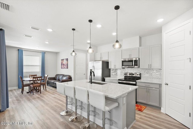 kitchen with appliances with stainless steel finishes, light wood-type flooring, light stone counters, sink, and an island with sink