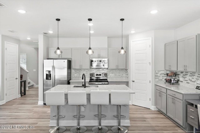 kitchen with an island with sink, light hardwood / wood-style floors, decorative light fixtures, and appliances with stainless steel finishes