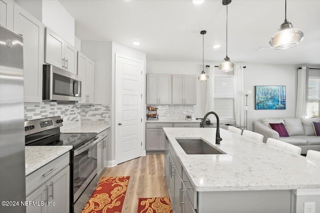 kitchen featuring decorative light fixtures, sink, stainless steel appliances, and an island with sink