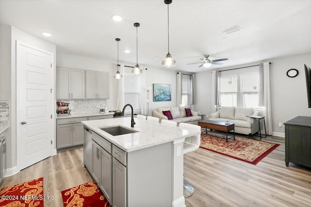 kitchen with sink, light stone counters, an island with sink, light hardwood / wood-style floors, and gray cabinets