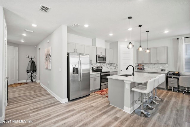 kitchen featuring sink, stainless steel appliances, light hardwood / wood-style flooring, decorative light fixtures, and a center island with sink