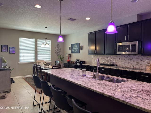 kitchen with light tile patterned floors, tasteful backsplash, stainless steel microwave, a sink, and black electric cooktop