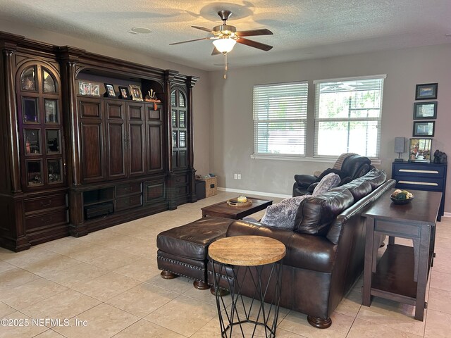 living area with light tile patterned floors, baseboards, a ceiling fan, and a textured ceiling