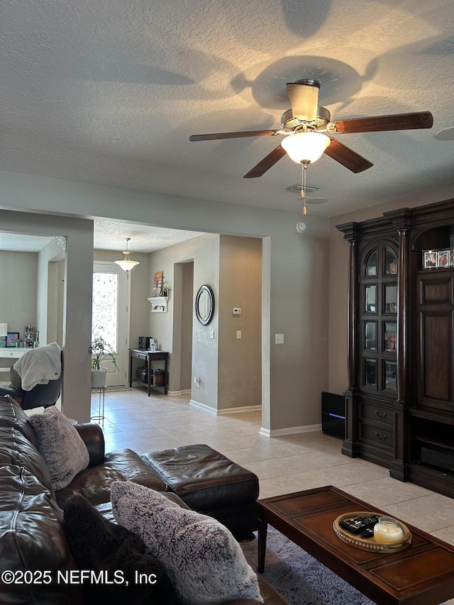 living area featuring a textured ceiling, light tile patterned flooring, baseboards, and a ceiling fan