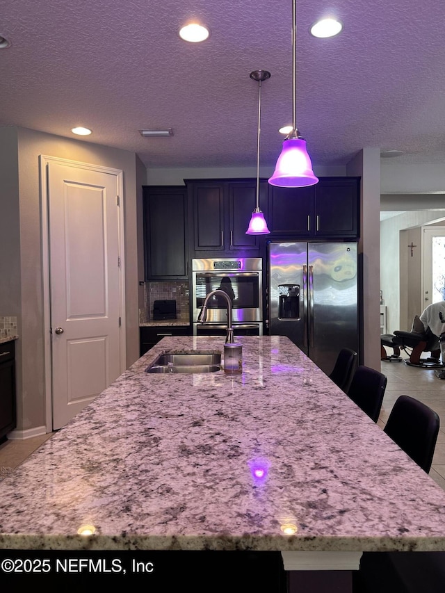 kitchen featuring light stone countertops, a kitchen breakfast bar, a sink, stainless steel fridge, and decorative light fixtures