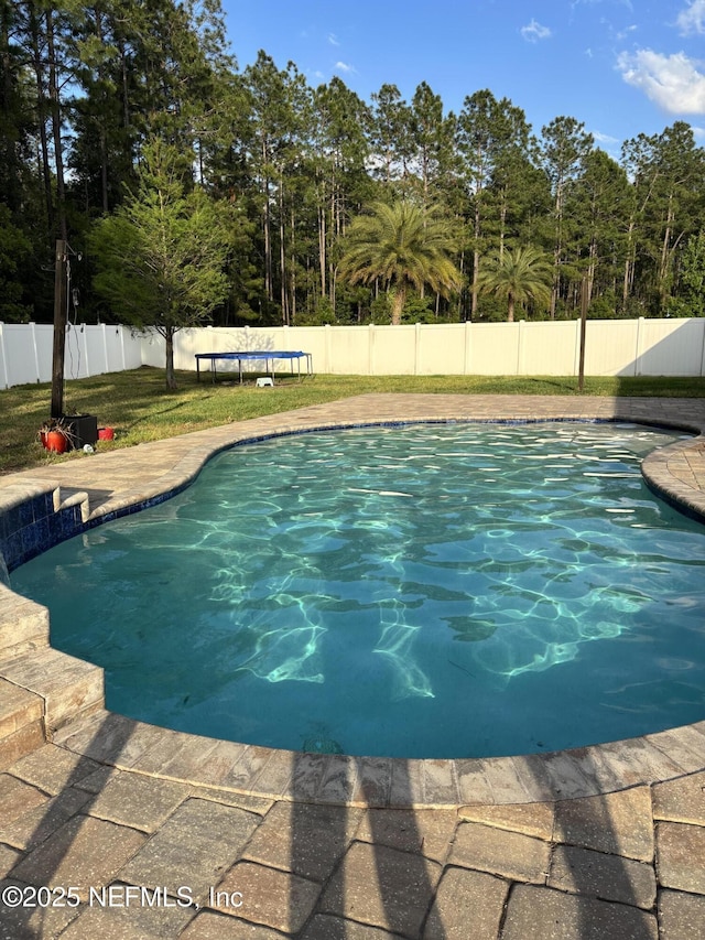 view of swimming pool featuring a fenced backyard, a trampoline, a fenced in pool, and a lawn