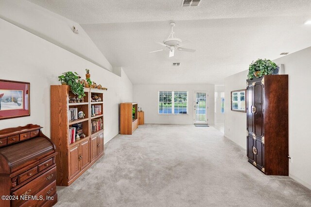 interior space with light carpet, a textured ceiling, vaulted ceiling, and ceiling fan