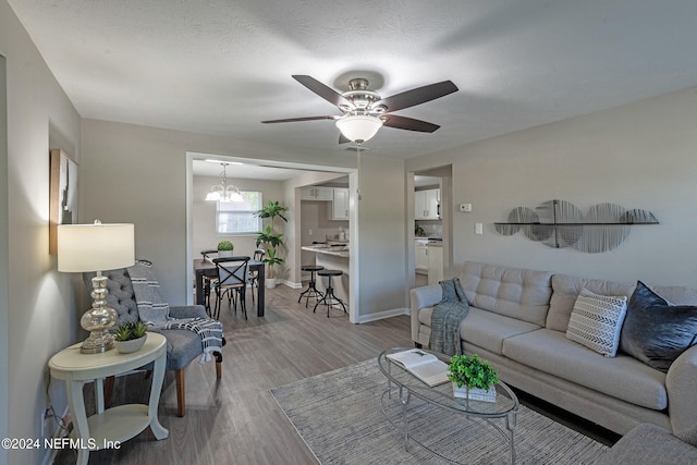 living room featuring light hardwood / wood-style flooring, ceiling fan with notable chandelier, and a textured ceiling