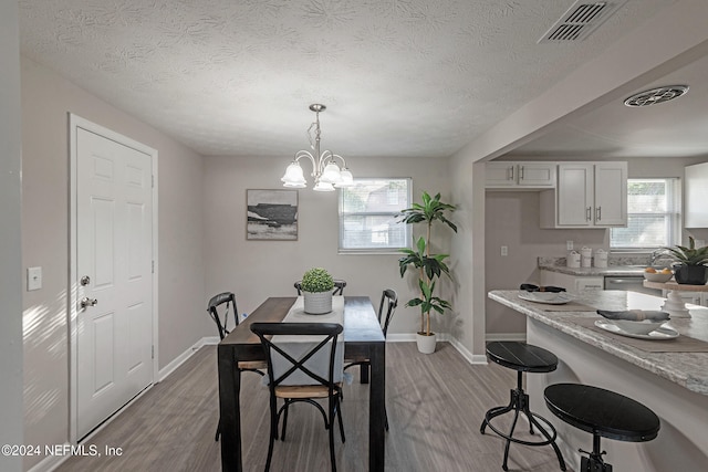 dining area featuring light hardwood / wood-style flooring, a textured ceiling, and an inviting chandelier