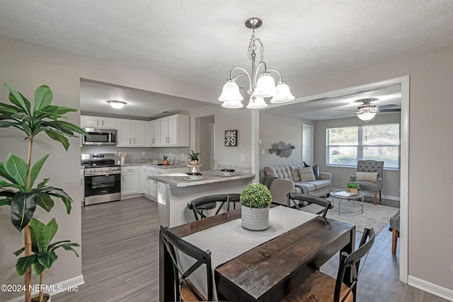 dining area with ceiling fan with notable chandelier, wood-type flooring, and a textured ceiling