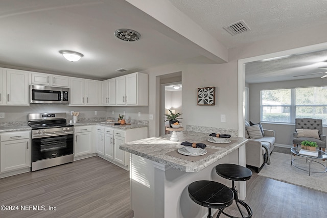 kitchen with a breakfast bar, white cabinetry, kitchen peninsula, and stainless steel appliances