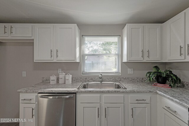 kitchen with stainless steel dishwasher, light stone counters, white cabinetry, and sink