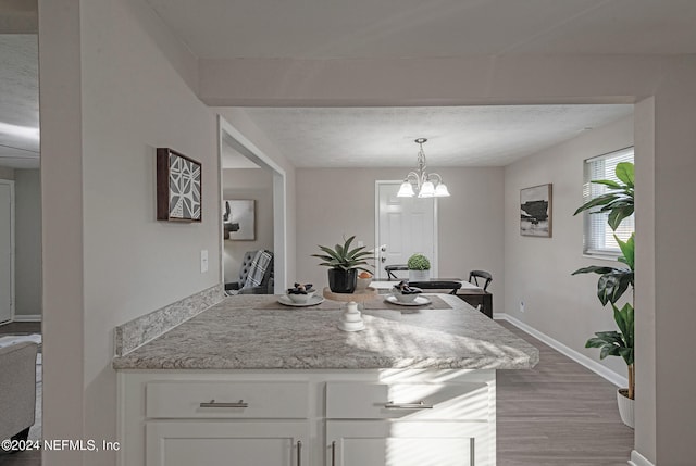 kitchen featuring light stone countertops, decorative light fixtures, hardwood / wood-style flooring, a notable chandelier, and white cabinets