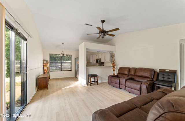 living room with ceiling fan with notable chandelier, light hardwood / wood-style floors, and vaulted ceiling