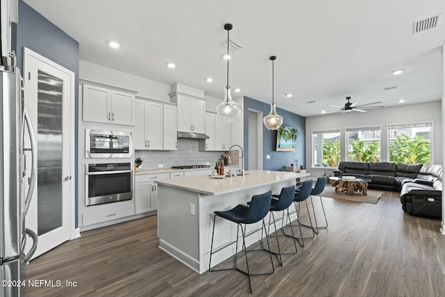 kitchen with white cabinetry, ceiling fan, hanging light fixtures, a center island with sink, and appliances with stainless steel finishes