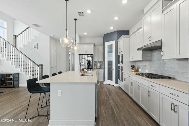 kitchen with pendant lighting, a center island with sink, dark hardwood / wood-style flooring, white cabinetry, and stainless steel appliances