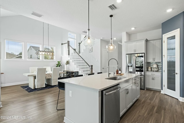 kitchen with a kitchen island with sink, dark wood-type flooring, sink, appliances with stainless steel finishes, and decorative light fixtures