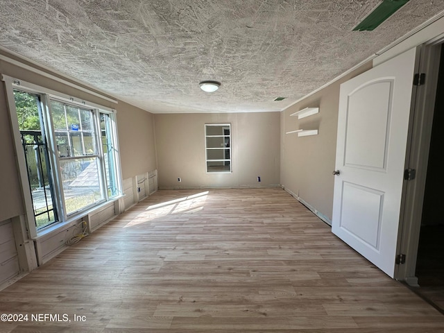 empty room featuring a textured ceiling, light wood-type flooring, and a healthy amount of sunlight