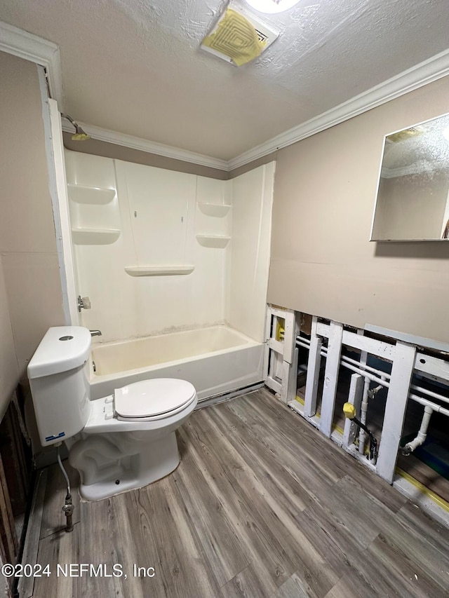 bathroom with washtub / shower combination, hardwood / wood-style flooring, toilet, ornamental molding, and a textured ceiling