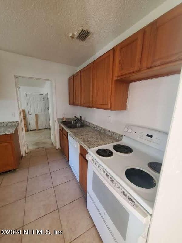 kitchen featuring a textured ceiling, light tile patterned flooring, white appliances, and sink