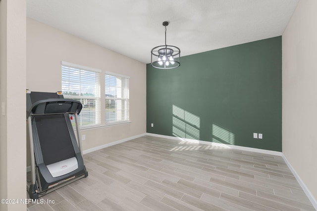 exercise room with light wood-type flooring and an inviting chandelier