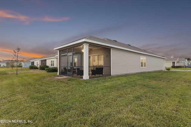 back house at dusk with a yard and a sunroom