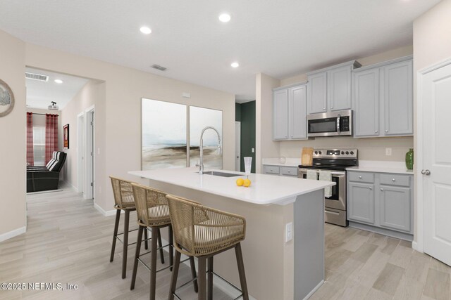 kitchen featuring stainless steel appliances, gray cabinetry, a kitchen island with sink, and sink