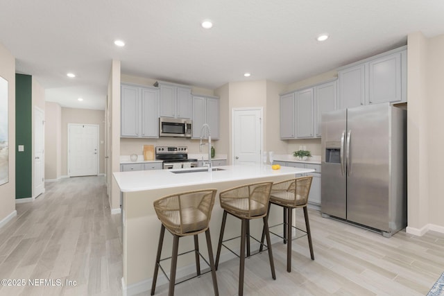 kitchen with an island with sink, light wood-type flooring, sink, appliances with stainless steel finishes, and a kitchen bar