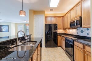 kitchen featuring backsplash, dark stone counters, sink, black appliances, and decorative light fixtures