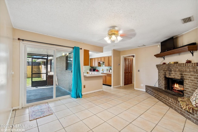 unfurnished living room with ceiling fan, light tile patterned flooring, a textured ceiling, and a brick fireplace