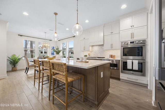 kitchen with a center island with sink, white cabinetry, hanging light fixtures, and appliances with stainless steel finishes