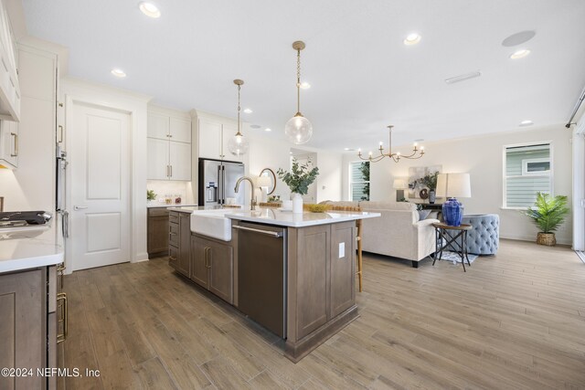 kitchen with white cabinetry, decorative light fixtures, a center island with sink, appliances with stainless steel finishes, and light wood-type flooring